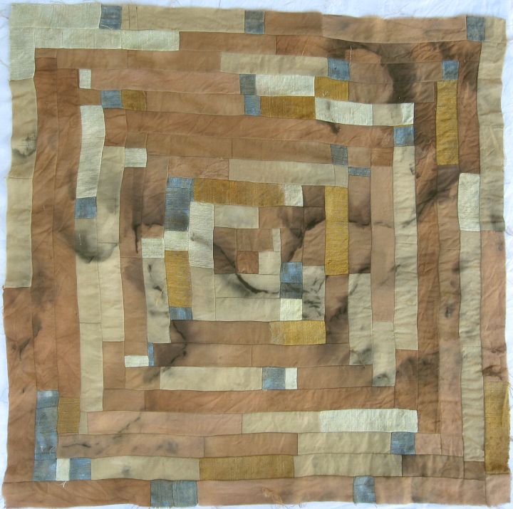 A log-cabin patchwork of wool fabric, dyed in shades of brown, yellow, grey and indigo and marked with black rust marks.