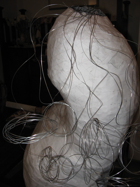 The white paper-covered form with several long lengths of wire attached at the top and hanging down in coils.