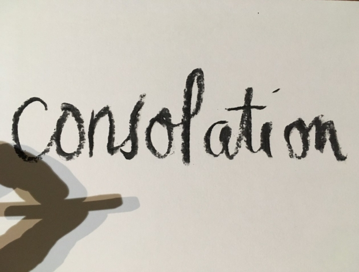 The word 'consolation' handwritten in thick black graphite on white paper, with a shadow of fingers holding the graphite stick cast on the paper.
