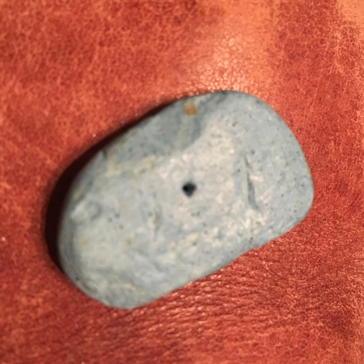 An out of focus grey-blue old eraser with a hole in the centre, lying on red leather.