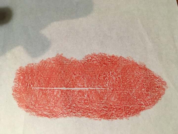 A roughly coloured in mouth-shaped patch of red crayon, drawn on white rice paper, with a cast shadow in the top left corner.